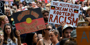 Demonstranten zeigen Schilder, auf einem steht „Der australische Traum wurzelt in Rassismus“