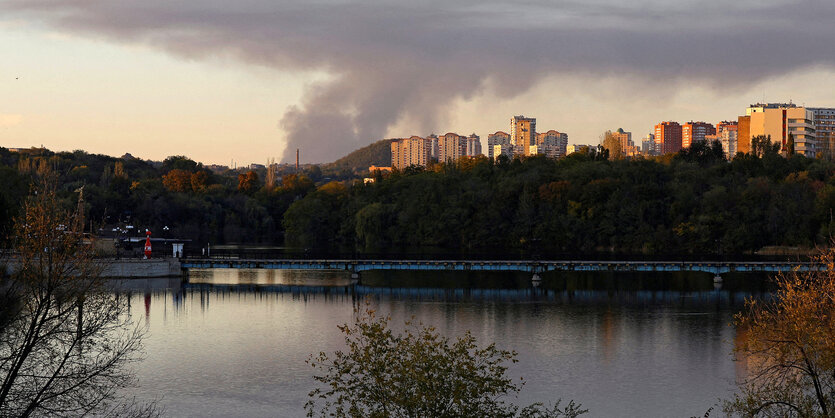 Rauch steigt über einer Stadtsilhouette am Ufer eines Gewässers auf