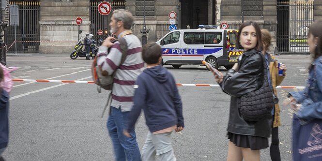 Menschen stehen zwischen Polizeiabsperrungen auf einer Straße