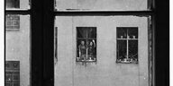 menschen schauen aus einem Fenster und winken in einen Kreutbeerger HInterhof