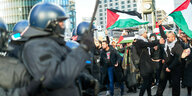 Polizisten stehen mit Schlagstöcken vor Demonstranten die mit Palästina Flaggen unterwegs und aufgebracht sind