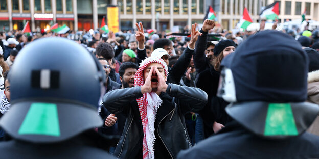 Ein Mann, der ein Palästinensertuch um den Kopf gewickelt hat, schreit zwei Polizisten an