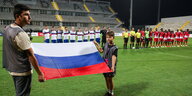 Teams stellen sich zur Nationalhymne auf, im Vordergrund halten zwei die russische Flagge