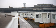 Ein Zaun trennt Wohncontainer vom Tempelhofer Feld, im Hintergrund das alte Flughafengebäude