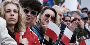 Menschen tragen Sonnenbrillen und halten Fähnchen in den nationalfarben polens in den Händen