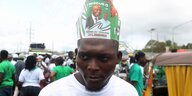 Ein Mann trägt einen Hut aus Papier, der mit dem Foto des Liberianischen Oppositionskandidaten verziert ist