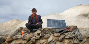 Eine Junge sitzt neben einem Solar Panel auf einer Steinmauer, im Hintergrund Gebirge