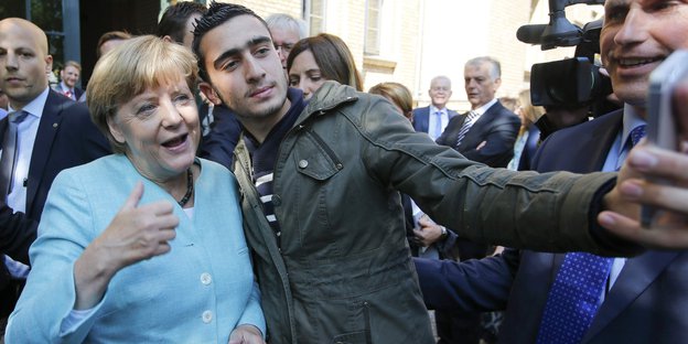 Angela Merkel und ein Flüchtling machen ein Selfie.