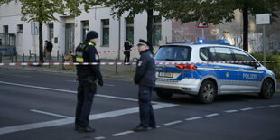 zwei Polizisten stehen auf der Straße. Im Hintergrund Häuser und ein Polizeiwagen