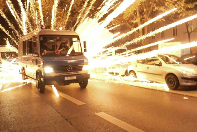 Ein Polizeiauto fährt, direkt dahinter zündet Feuerwerk