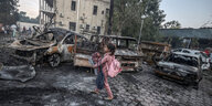 Ein Mädchen mit seinen Habseligkeiten neben ausgebrannten Autos in Gaza