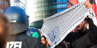 Eine Mann hält einem Polizisten ein Palästinensertuch entgegen
