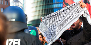Eine Mann hält einem Polizisten ein Palästinensertuch entgegen