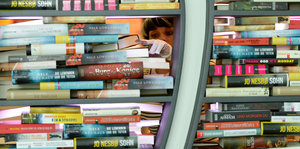 Eine Frau schaut durch eine Lücke in einer Bücherwand