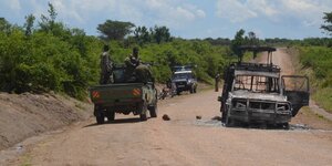 Ein ausgebranntes Auto und Soldaten auf einer Straße in einem Nationalpark in Uganda