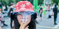 Eine Frau raucht, sie trägt einen roten Hut, der mit einem Muster aus Hanfbättern verziert ist