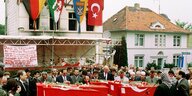fünf Särge mit türkischen Flaggen, umgeben von Mensche, vor einem abgebrannten Wohnhaus, an dem auch mehrere Flaggen hängen