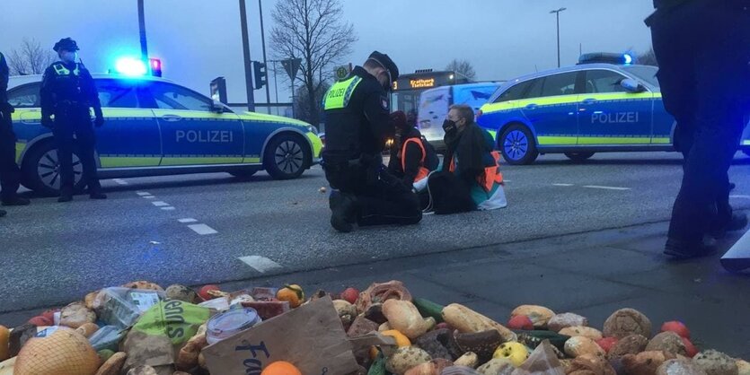 Essen liegt auf den Elbbrücken, im Hintergrund sitzt eine Aktivist*in mit gelber Weste, Polizeiwagen stehen auf der Straße