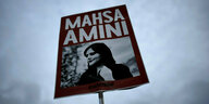 Ein Schild zeigt Mahsa Amini vor bewölktem Himmel