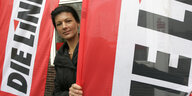 Sahra Wagenknecht steht zwischen zwei Fahnen mit dem Logo der Partei "Die Linke"
