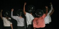 Theaterprobe: Frauen tragen kugelförmige Helme auf dem Kopf und recken die Faust nach oben