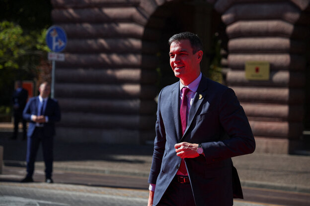 Spaniens Regierungschef Pedro Sánchez läuft bei Sonnenschein und Strahlen im Gesicht über eine Straße. mit seiner linken Hand greift er an den mittleren Knopf seiner Jacketts