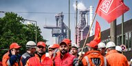 Arbeiter stehen vor einem Stahlwerk, einer schwenkt die Fahne der IGMetall