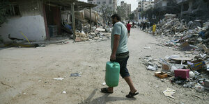 Ein mann mit Wasserkanister in einer Strasse voller Müll in Gaza