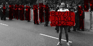 Der Künstler Paweł Żukowski hält auf einer Straße ein rotes Transparent, hinter ihm stehen Polizisten.