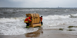 Feuerwehrleute tragen einen Strandkorb aus dem Wassser