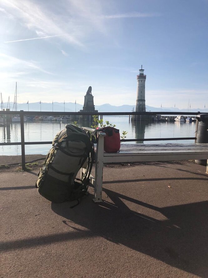 Rucksack lehnt an einer Bank, im Hintergrund der Hafen von Lindau