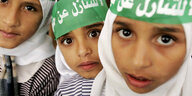Drei kleine palästinensische Mädchen tragen grüne Hamas-Stirnbänder und blicken in die Kamera.