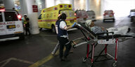 Eine Person wird auf einer Liege geschoben, im Hintergrund Krankenwagen