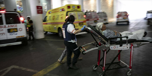 Eine Person wird auf einer Liege geschoben, im Hintergrund Krankenwagen