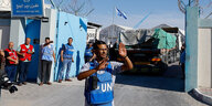 Ein Mann steht vor dem Eingang eines UN-Lagers im Gazastreifen und macht Handzeichen, dahinter das Eingangstor, durch das gerade ein Truck gefahren ist