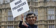 Eine Puppe mit Ähnlichkeit zum britischen Premier Sunak hält ein Schild hoch auf dem steht: Make Polluters Pay