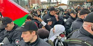 Polizisten um eine Frau mit Palästina-Flagge