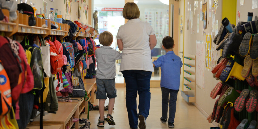 Eine Erzieherin geht im Kindergarten mit zwei Kindern über den Flur der Einrichtung.