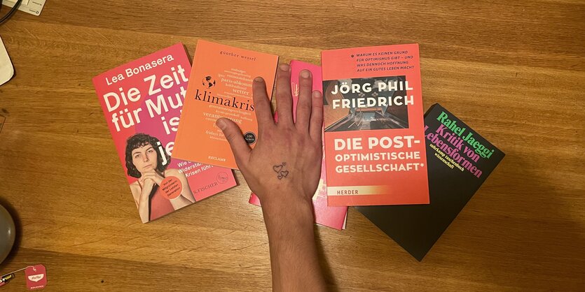 Eine Hand greift über einige Bücher, die auf einem Tisch liegen