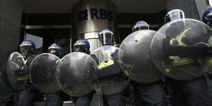 Britischen Polizist:innen in Riotgear mit runden Schilden stehen in einer Reihe vor der Royal Bank of Scottland während der G20-Proteste dort im Jahr 2009.