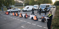 Polizeibeamte stehen während einer Straßenblockade der Klimaschutzgruppe Letzte Generation rund um die Aktivisten, die auf der Straße kleben