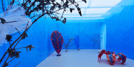 Blick in die Ausstellung: Blumen aus Pappmaché stehen in einem blau abgedunkelten Raum