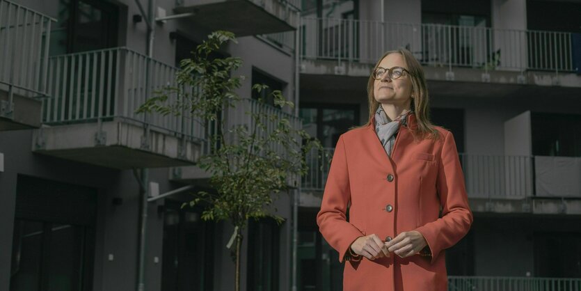 Anna Kreye steht mit orangenen Mantel vor einem Wohnhaus