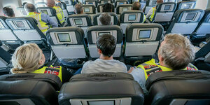 Ein mann sitzt zwischen einer Polizeibeamtin und einem Polizeibeamten in einem Flugzeug