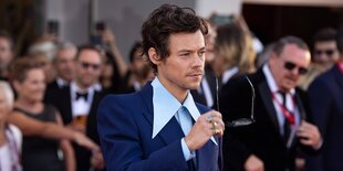 Harry Styles hältseine Sonnenbrille in der Hand