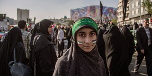 Eine junge Frau mit schwarzem Kopftuch und grünem Stirnband hat sich die Farben der Palästina-Fahne auf die Wangen gemalt