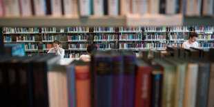 Besucher der Amerika Gedenkbibliothek in Berlin sitzen zwischen Bücherregalen.