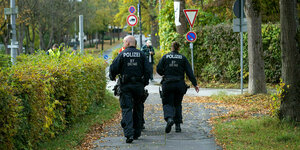 Zwei Polizisten von hinten laufen einen Gehweg entlang.