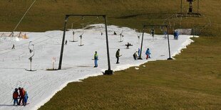 Skilift mit wenig Schnee auf einer grünen Wiese