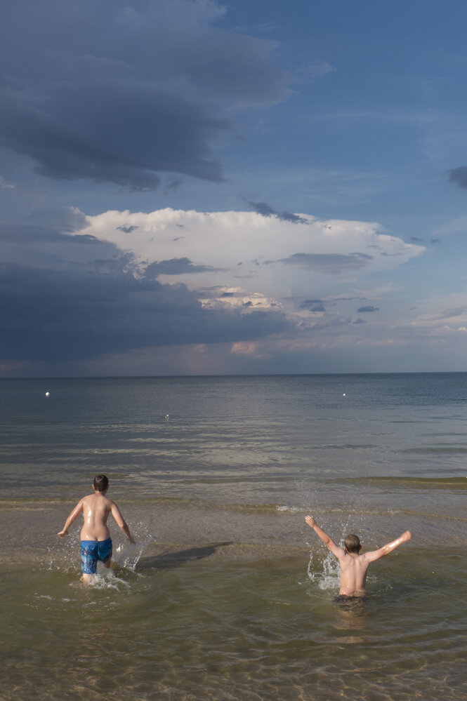 Zwei Jungen springen vor einem dunklen Himmel ins Meer